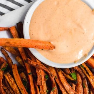 An aerial view of a plate of baked carrot fries with a fry dipped into sriracha mayo.