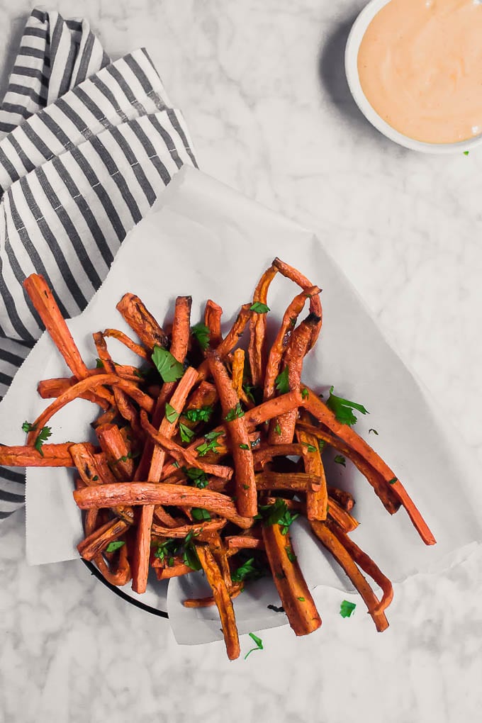 Aerial view of a basket of carrot fries and a bowl of sriracha mayo on a marble table. 