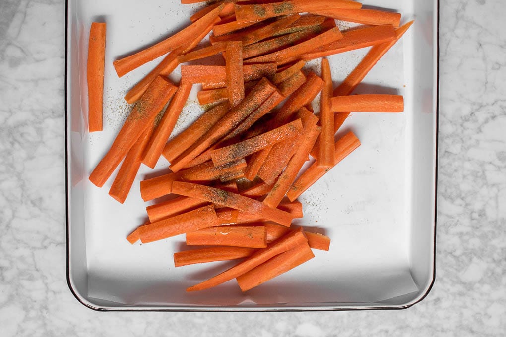 An aerial view of carrots on a baking sheet with spices and oil ready to be baked in the oven. 