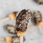 View of a frozen banana on a stick that's covered in chocolate, peanut butter and roasted salted peanuts