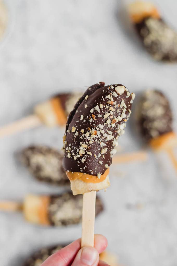 View of a frozen banana on a stick that's covered in chocolate, peanut butter and roasted salted peanuts