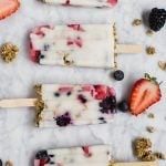 Aerial view of dairy-free yogurt and granola breakfast parfait popsicles with scattered berries and gluten-free granola.