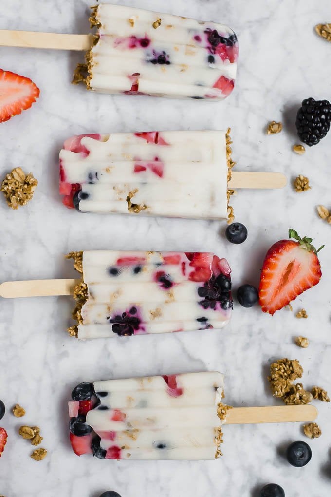 Aerial view of dairy-free yogurt and granola breakfast parfait popsicles with scattered berries and gluten-free granola. 