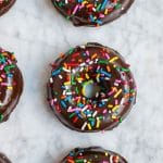 An aerial view of chocolate donuts with sprinkles on a marble table.