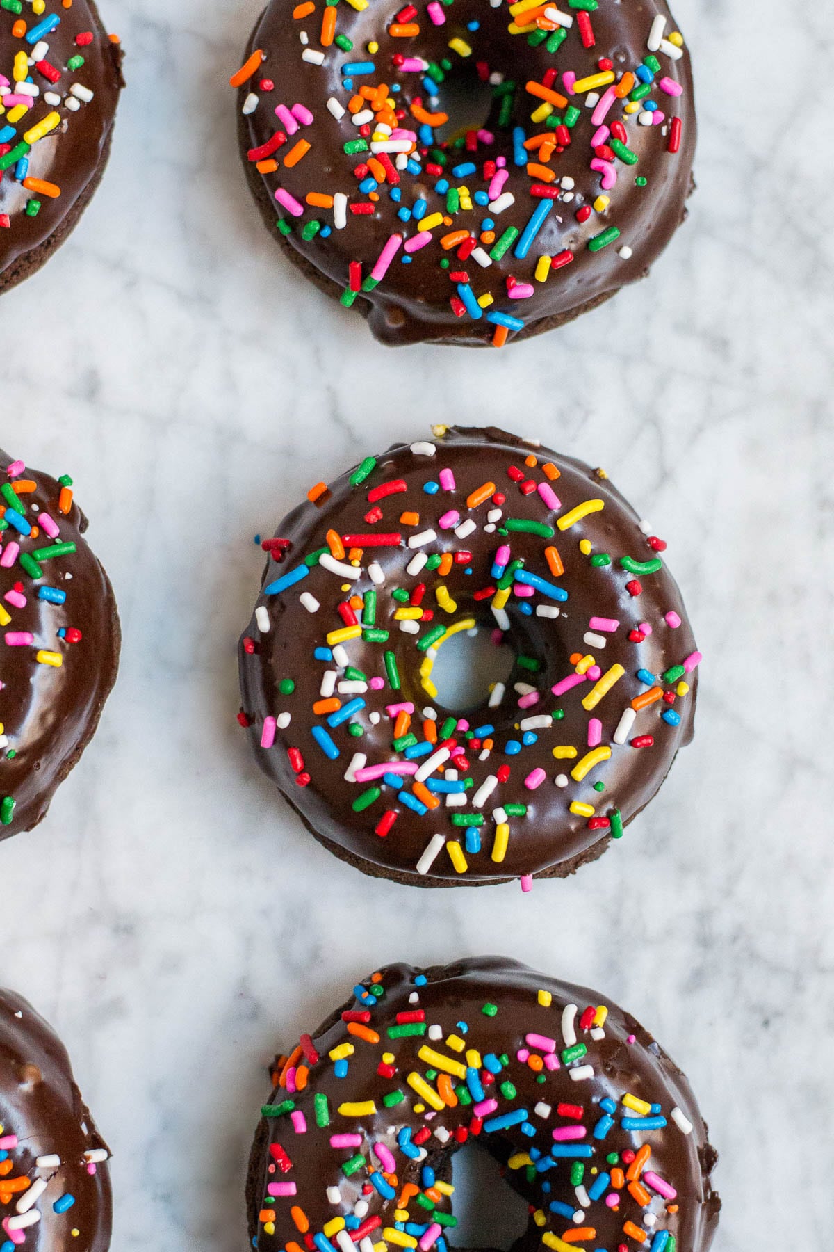 An aerial view of chocolate donuts with sprinkles on a marble table.