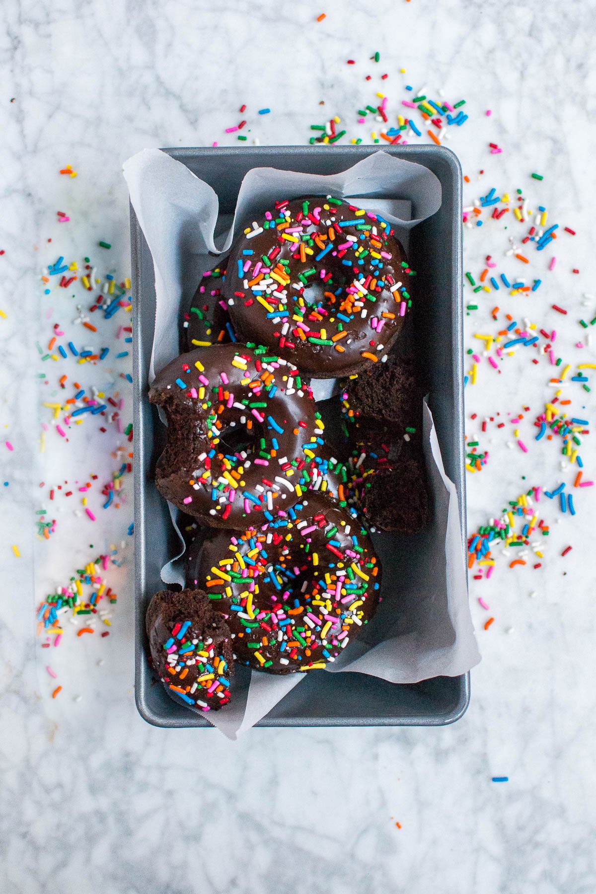An aerial view of gluten-free vegan chocolate donuts with sprinkles in a metal loaf pan 