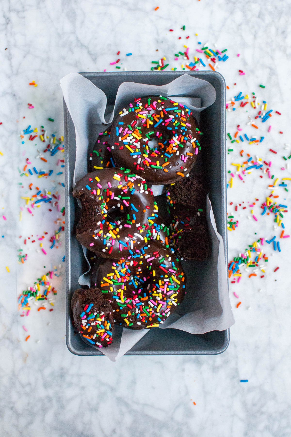 An aerial view of gluten-free vegan chocolate donuts with sprinkles in a metal loaf pan