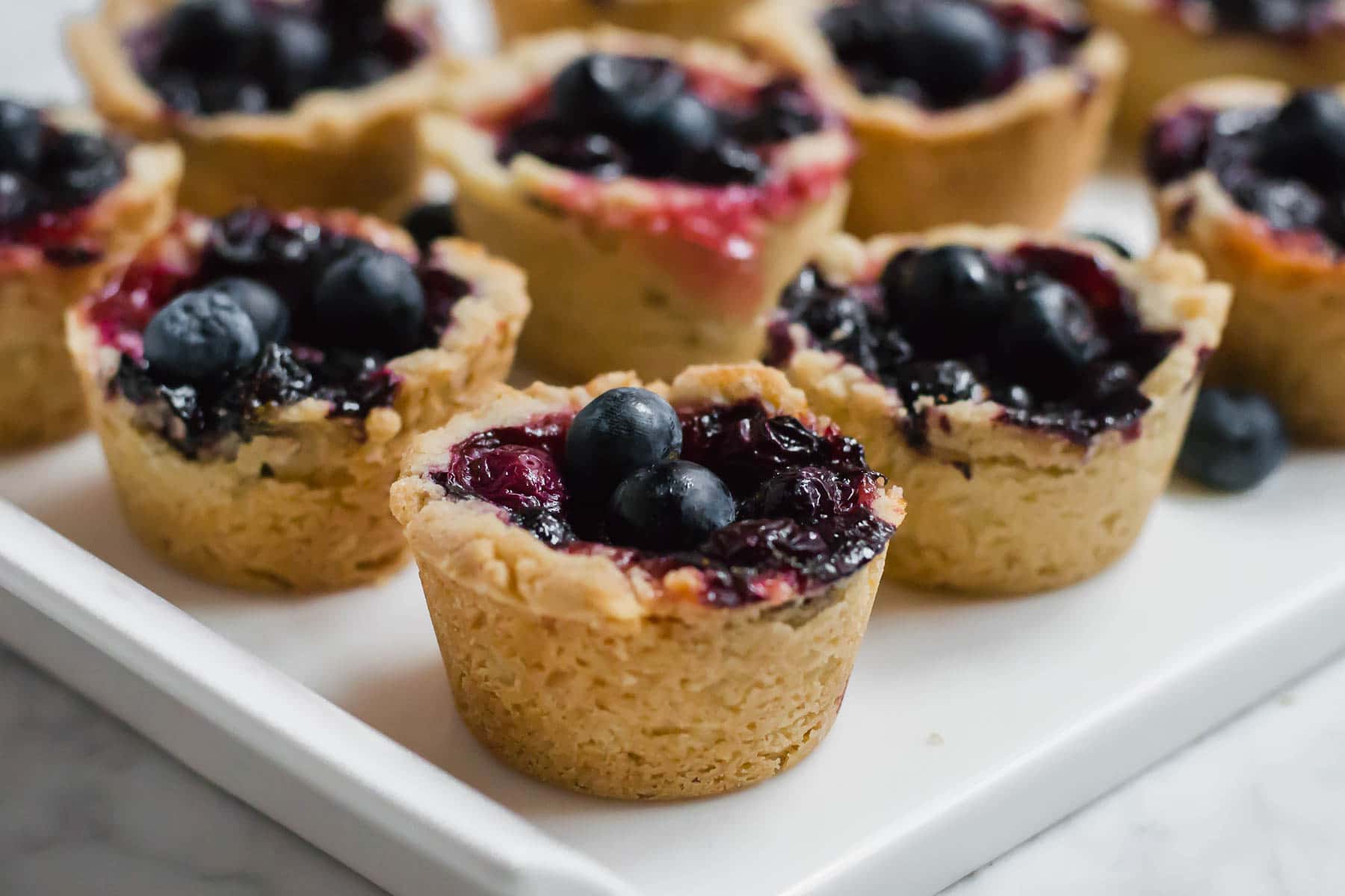 Rows of gluten-free mini blueberry tarts with a cookie crust on a serving plate