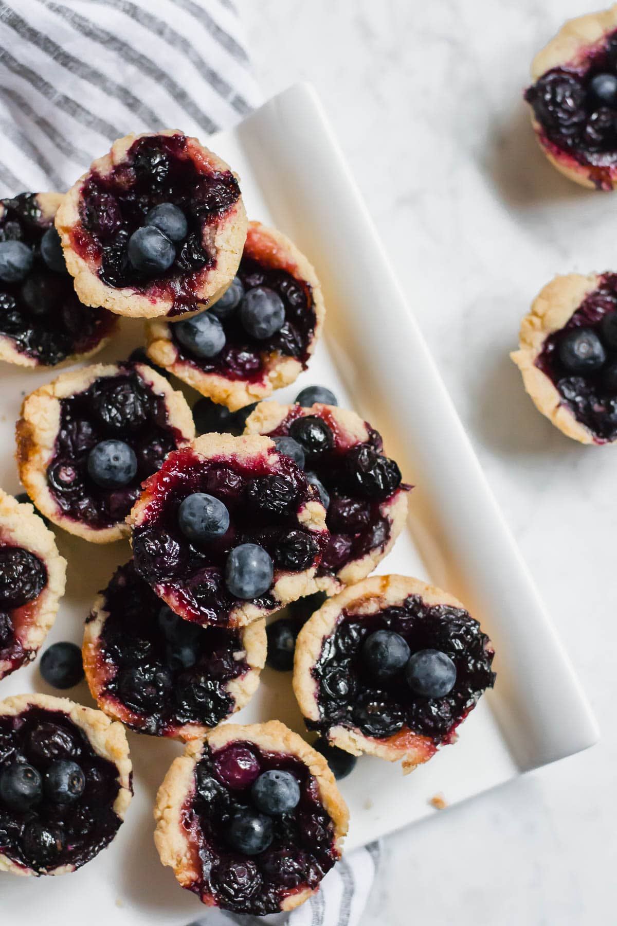 An aerial view of mini blueberry tarts on a serving dish with fresh blueberries. 