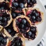 Aerial view of a plate of gluten-free mini blueberry tarts on a striped napkin.