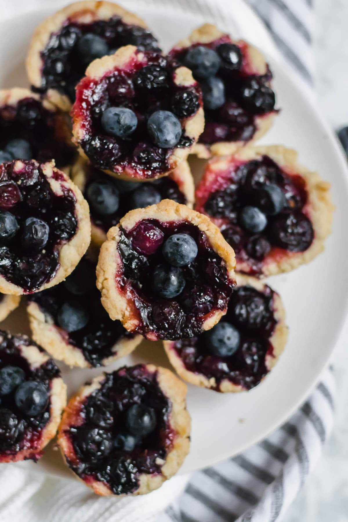 Aerial view of a plate of gluten-free mini blueberry tarts on a striped napkin. 