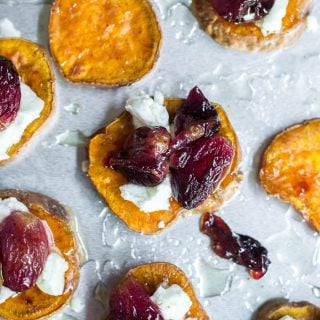 An aerial view of a baking sheet with sweet potato rounds topped with goat cheese, roasted grapes and a drizzle of honey.