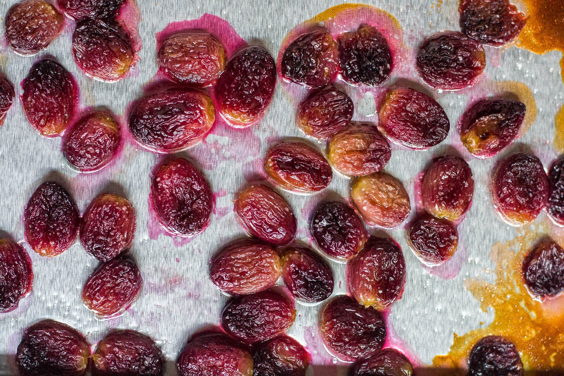 An aerial view of a baking sheet with roasted grapes tossed in oil and a pinch of sea salt.