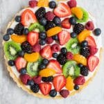 Aerial view of a round fruit tart with gluten-free shortbread crust and topped with blueberries, raspberries, strawberries, blackberries, kiwi and mandarin oranges