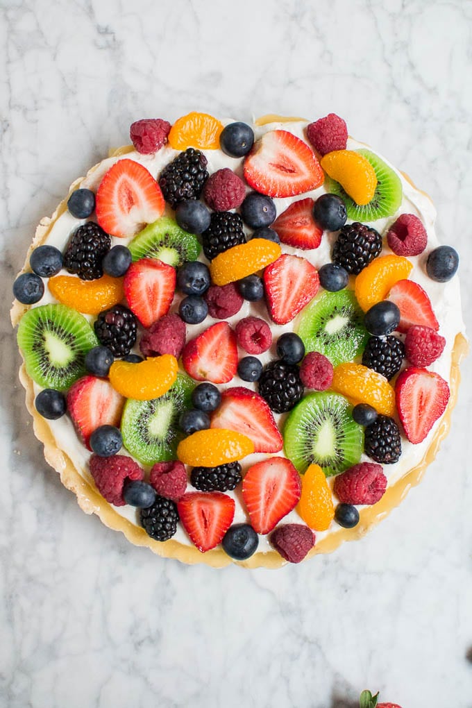 Aerial view of a round fruit tart with gluten-free shortbread crust and topped with blueberries, raspberries, strawberries, blackberries, kiwi and mandarin oranges