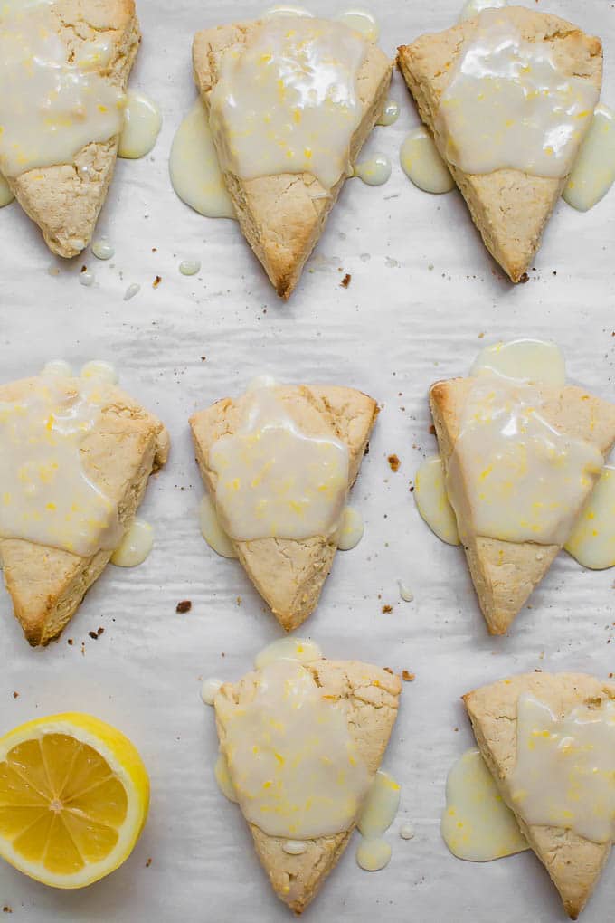 An aerial view of lemon scones on white parchment paper with fresh lemon glaze dripping off the sides. 