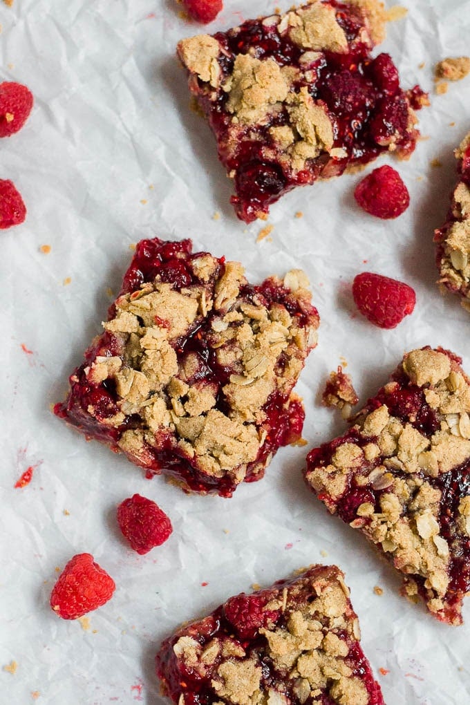 An aerial view of gluten-free vegan raspberry crumb bars on white parchment paper