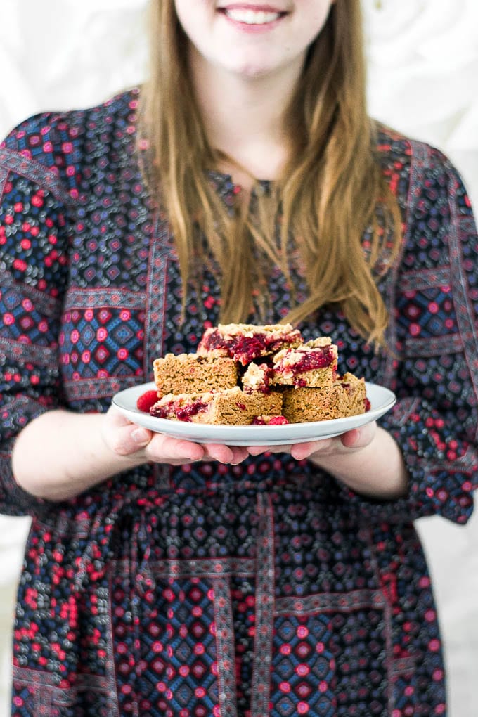 A straight on view of a woman holding a plate of gluten-free raspberry crumb bars. 