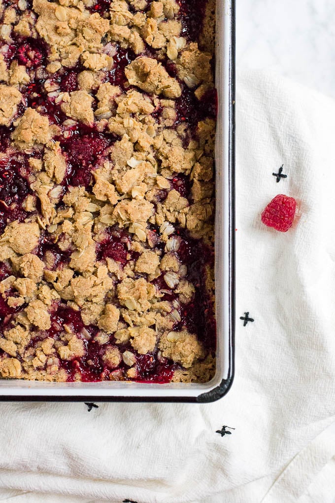 An aerial view of a pan with raspberry crumb bars with fresh raspberry on a white and black napkin. 