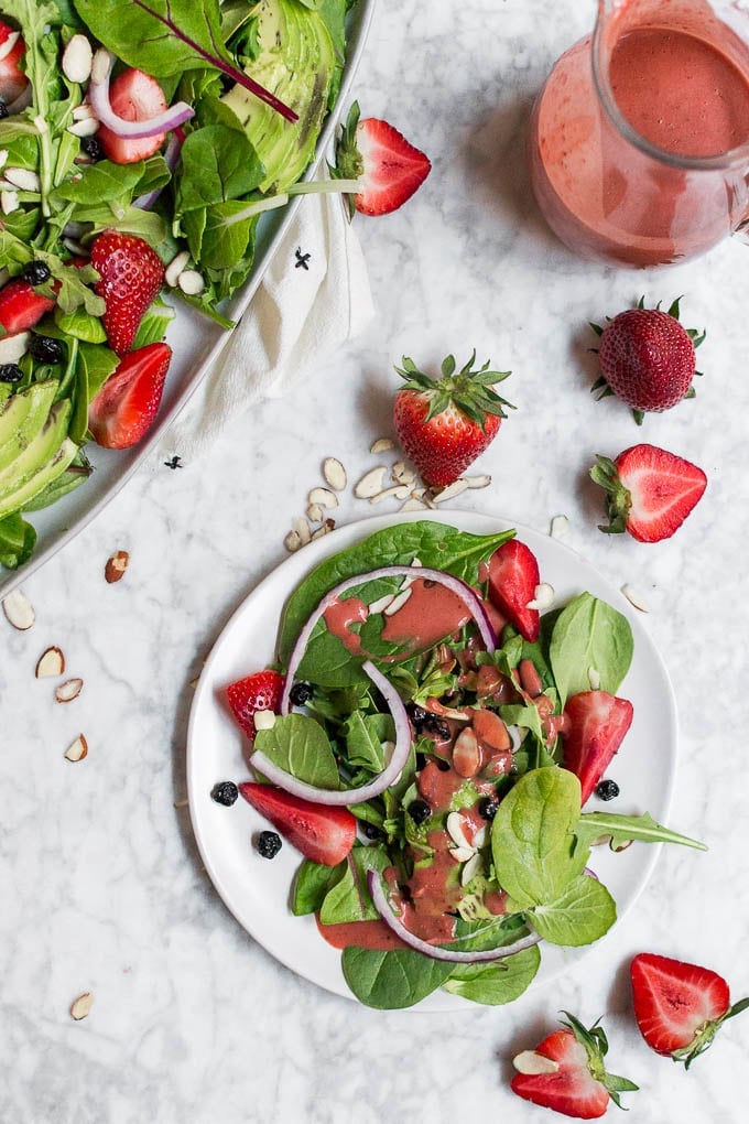 An aerial view of a plate of salad with strawberries and red onions with a bowl of dressing. 