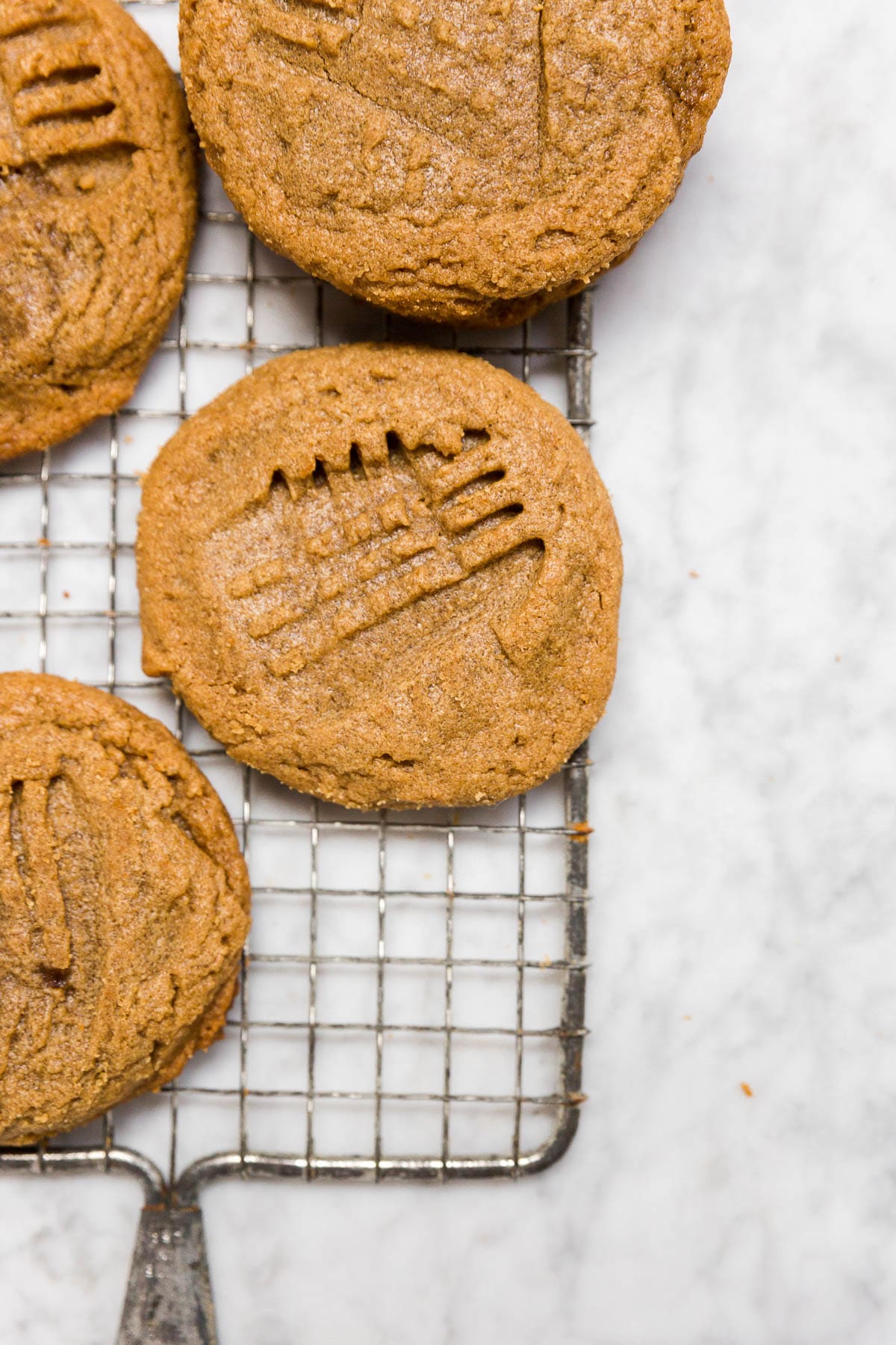 Aerial view of a wire cooling rack with gluten-free flourless peanut butter cookies with a cross-hatch pattern on a marble table. 