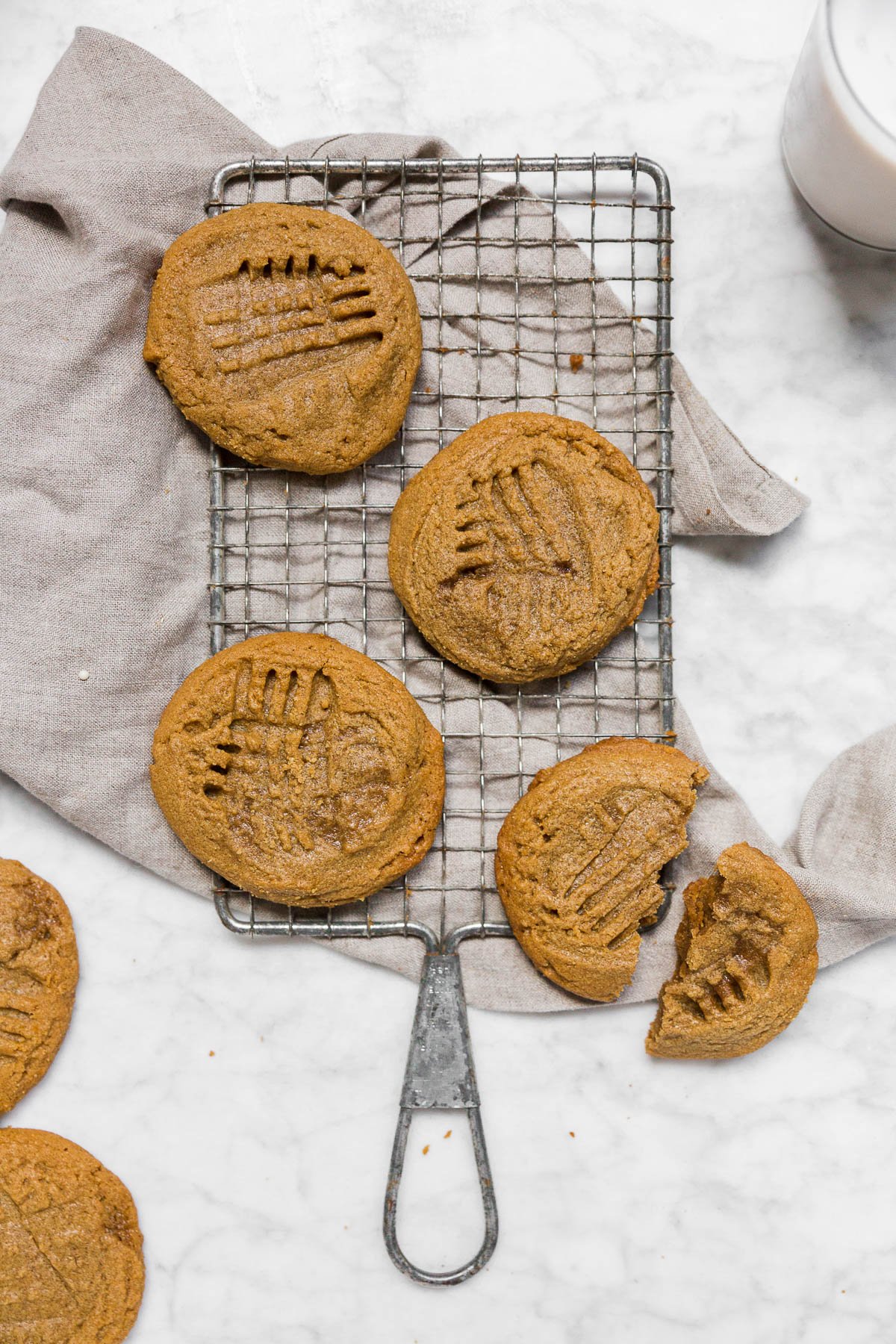 An aerial view of a cooling rack with 3-ingredient peanut butter cookies on a marble table with a gray napkin. 