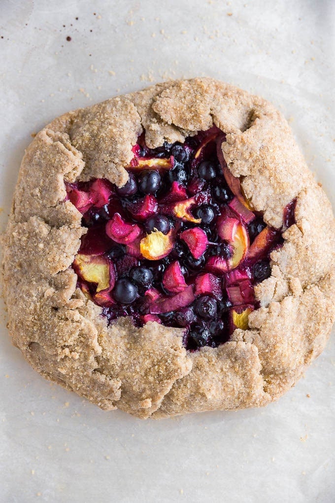 A gluten-free vegan rhubarb blueberry peach galette on a piece of parchment paper. 