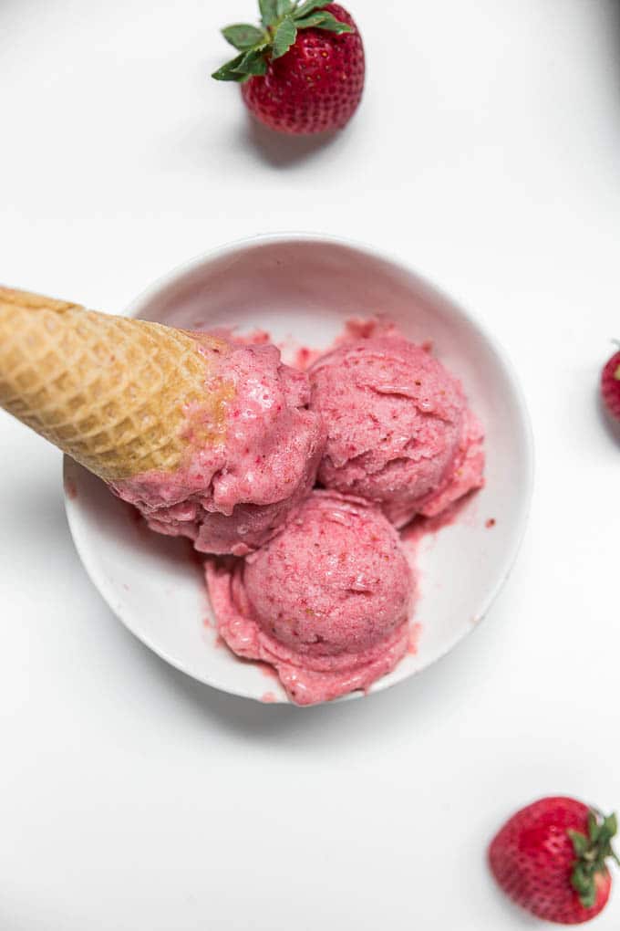A bowl of strawberry banana nice cream with a gluten-free cone and fresh strawberries