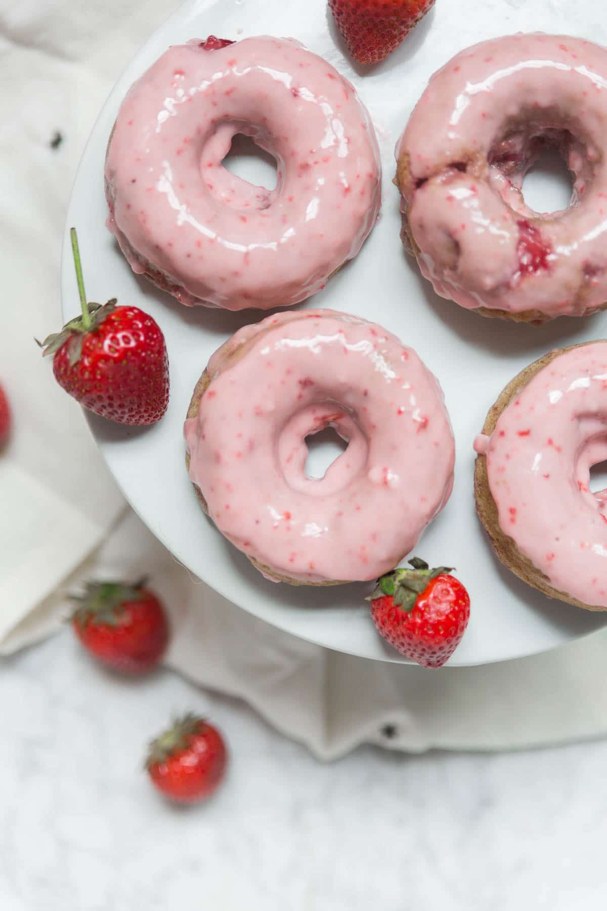 An aerial view of pink strawberry baked donuts with fresh strawberries on a cake platter. 