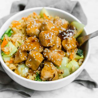 A bowl filled with cauliflower rice and chicken teriyaki with a fork.