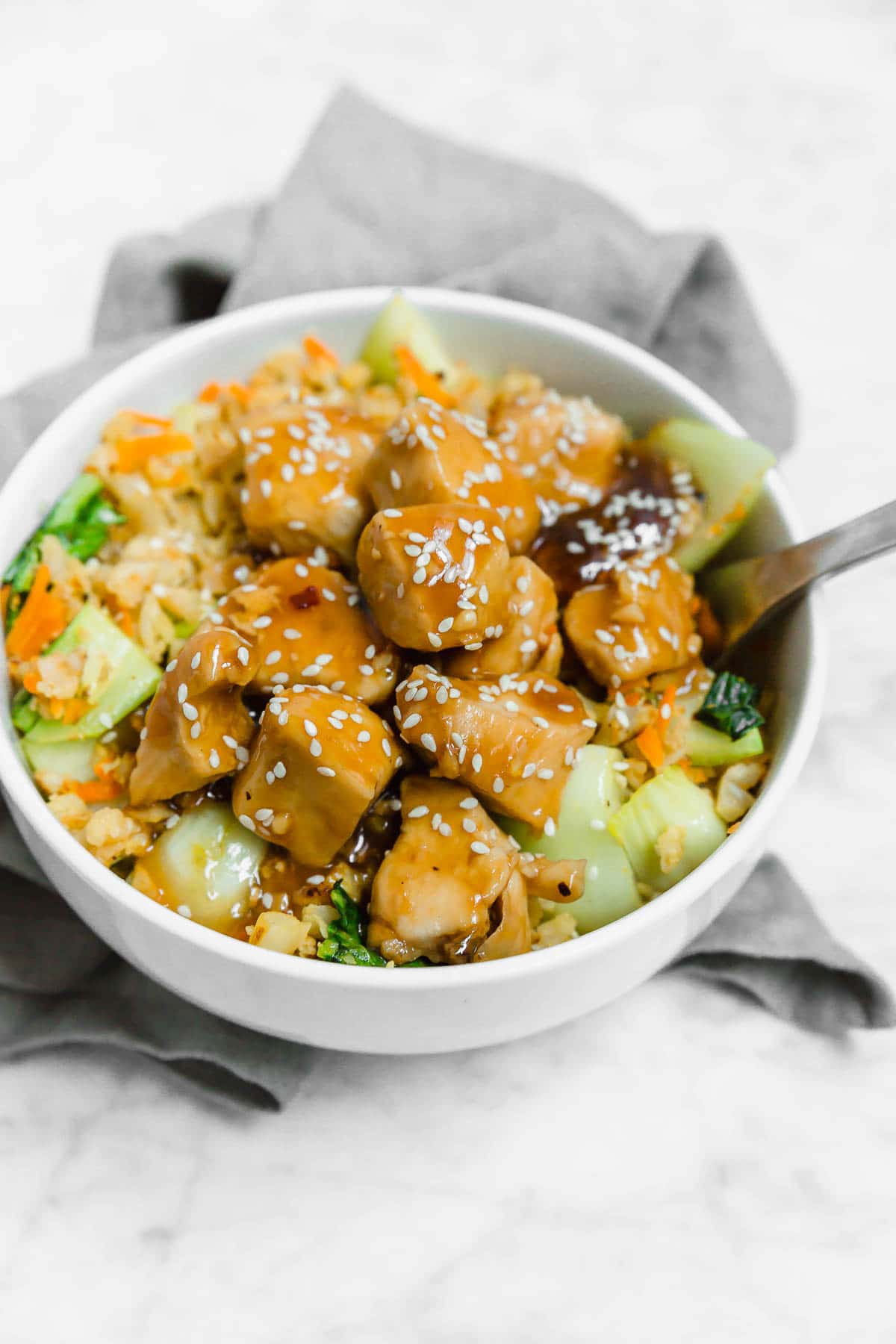 A bowl filled with cauliflower rice and chicken teriyaki with a fork. 