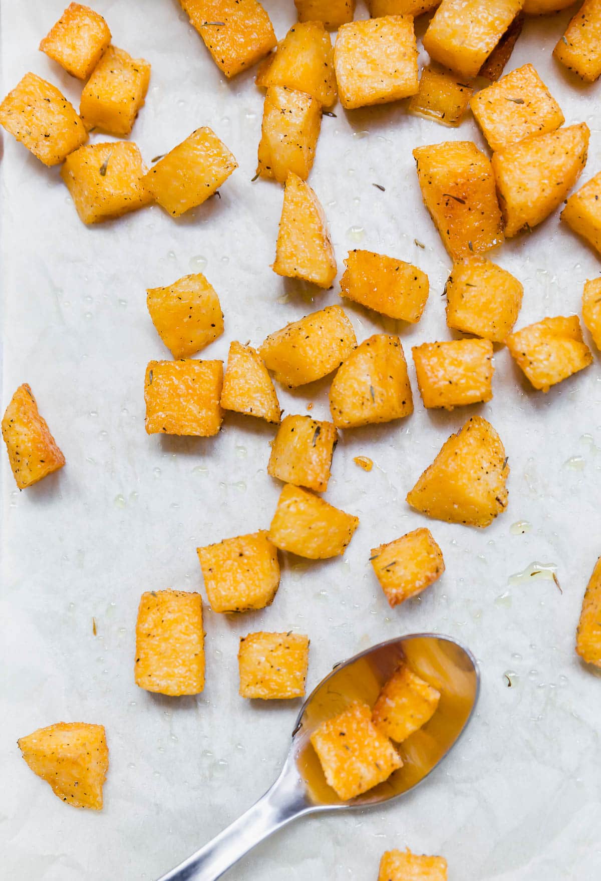 A sheet of parchment paper with polenta croutons and a spoon.