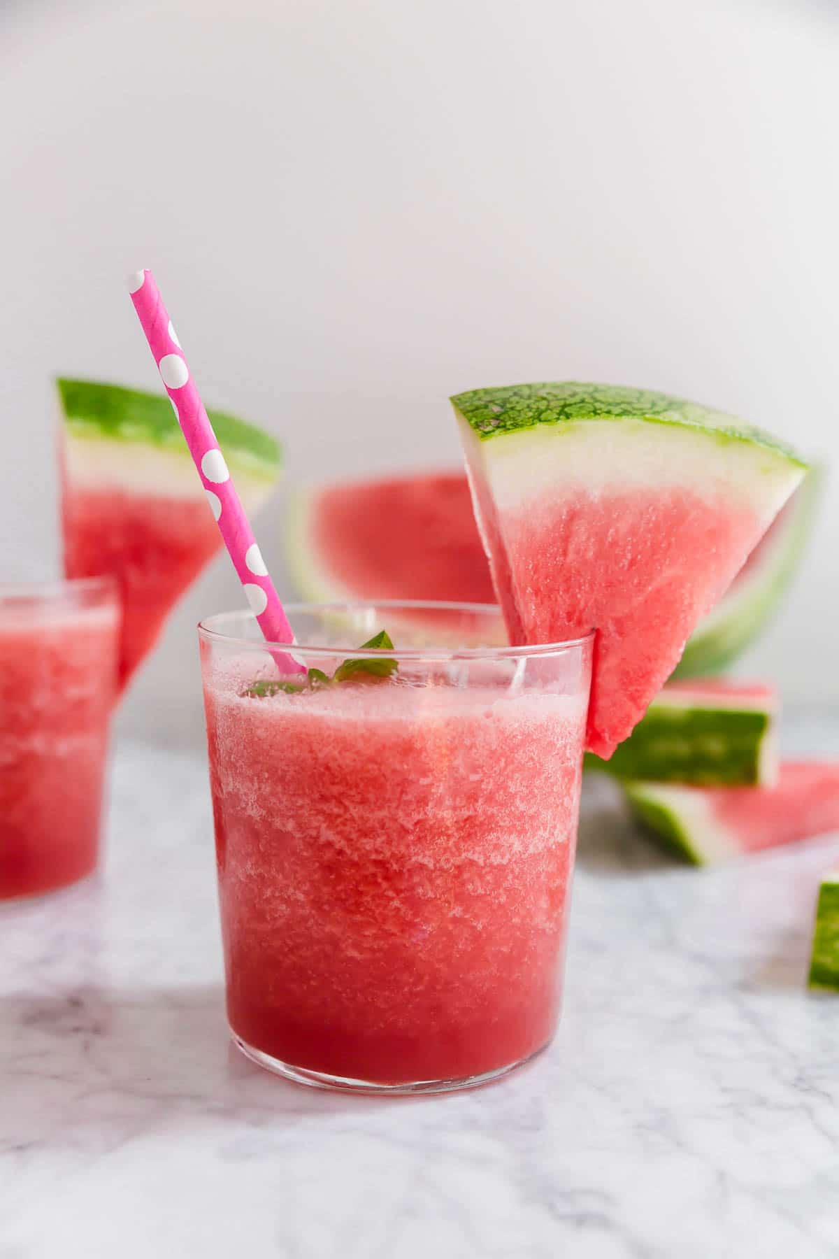A short glass with watermelon rosé slushie with a watermelon wedge and pink polka dot straw.