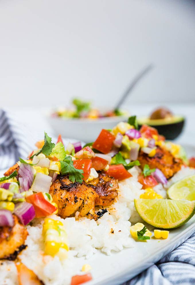 A plate of cod with blackened spices and tomato avocado corn salsa with lime.