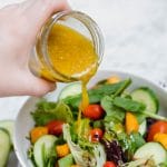 Gluten-Free honey mustard vinaigrette being poured onto a colorful salad.