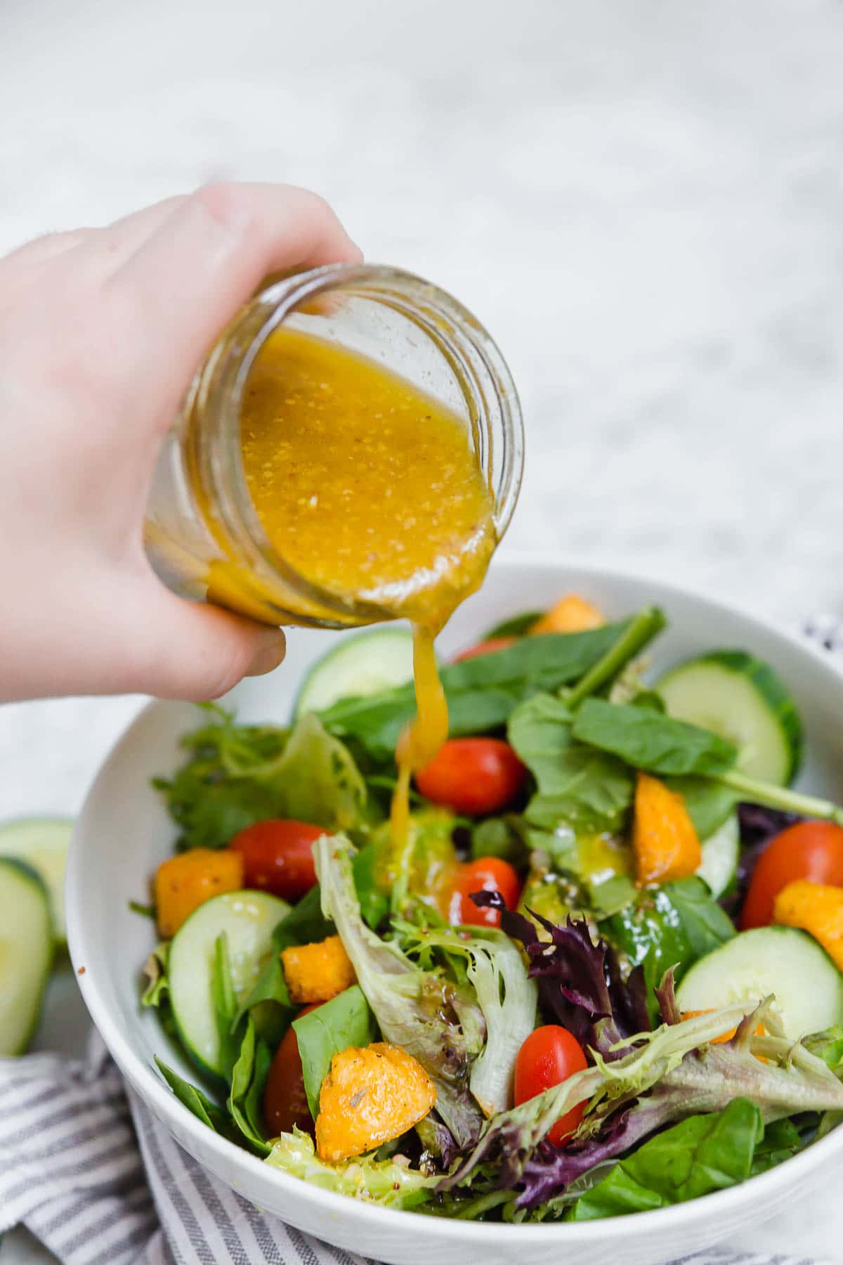 Gluten-Free honey mustard vinaigrette being poured onto a colorful salad. 