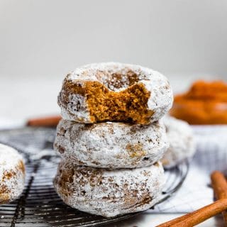 A stack of baked pumpkin donuts with cinnamon sticks.