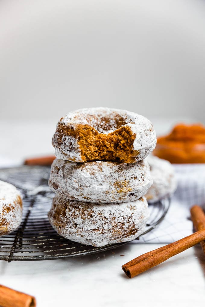 A stack of baked pumpkin donuts with cinnamon sticks. 