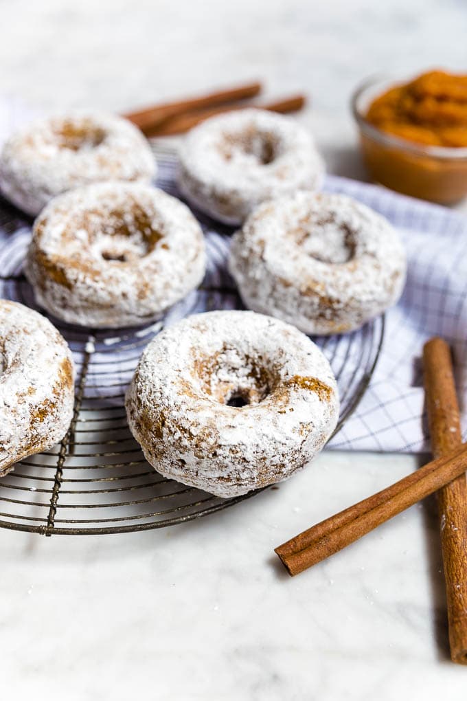 A wire rack of gluten-free vegan pumpkin donuts rolled in powdered sugar. 