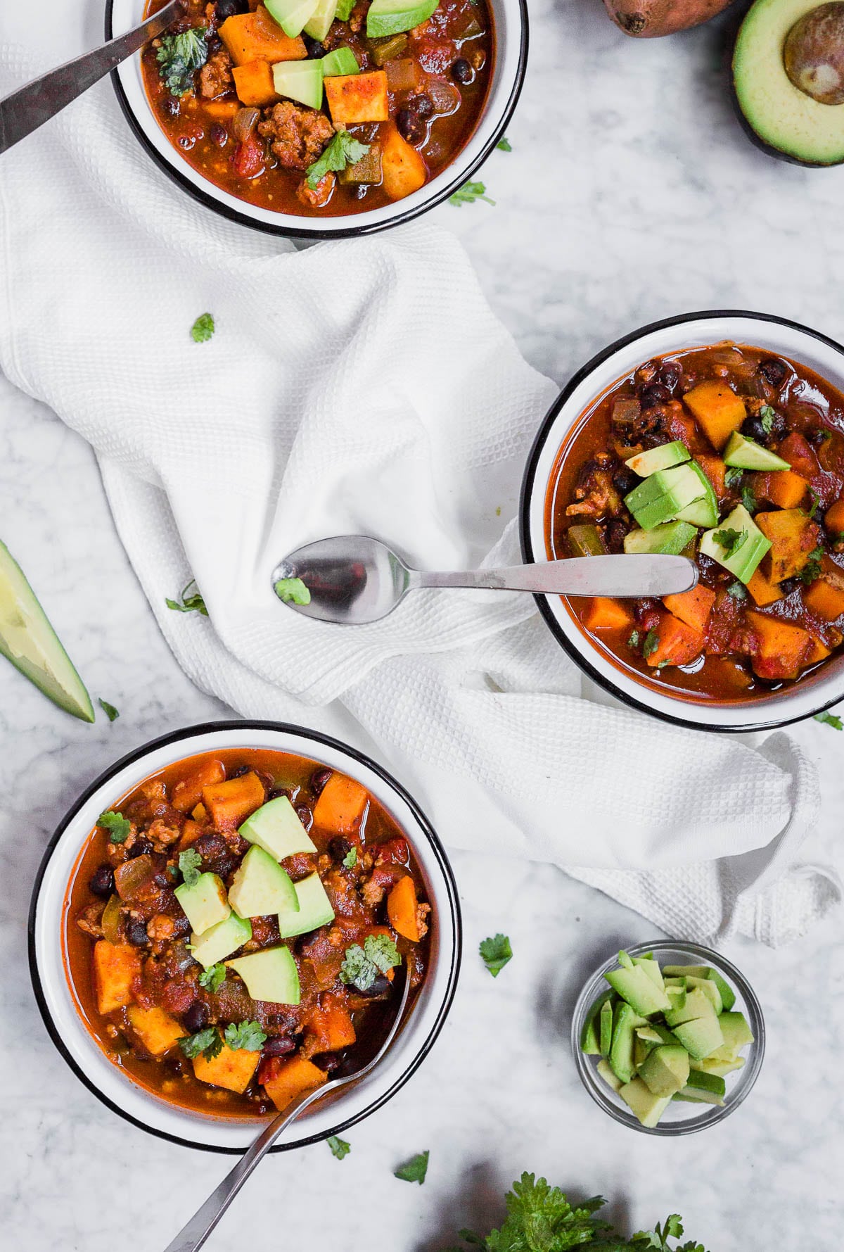 Three bowls of sweet potato turkey chili with avocado and cilantro.