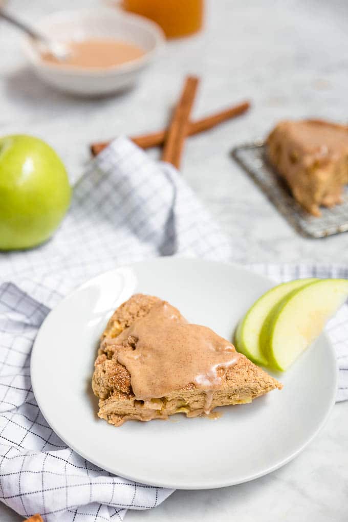 A plate with gluten-free vegan apple cinnamon scone with cinnamon apple glaze and slices of granny smith apple and cinnamon sticks. 