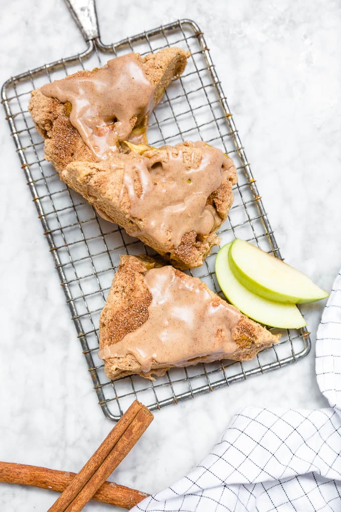 Gluten-Free vegan apple cinnamon scones on a cooling rack with granny smith apple slices and cinnamon sticks. 