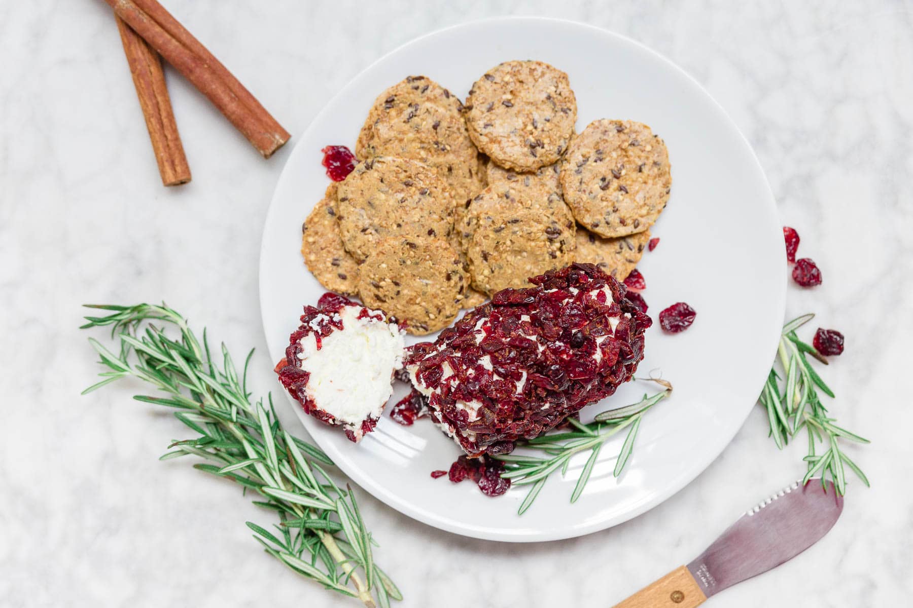 Plate of gluten-free crackers with cranberry rolled goat cheese log and cinnamon. 