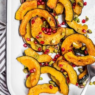 A white sheet pan with roasted acorn squash slices topped with pomegranate arils and pistachios.