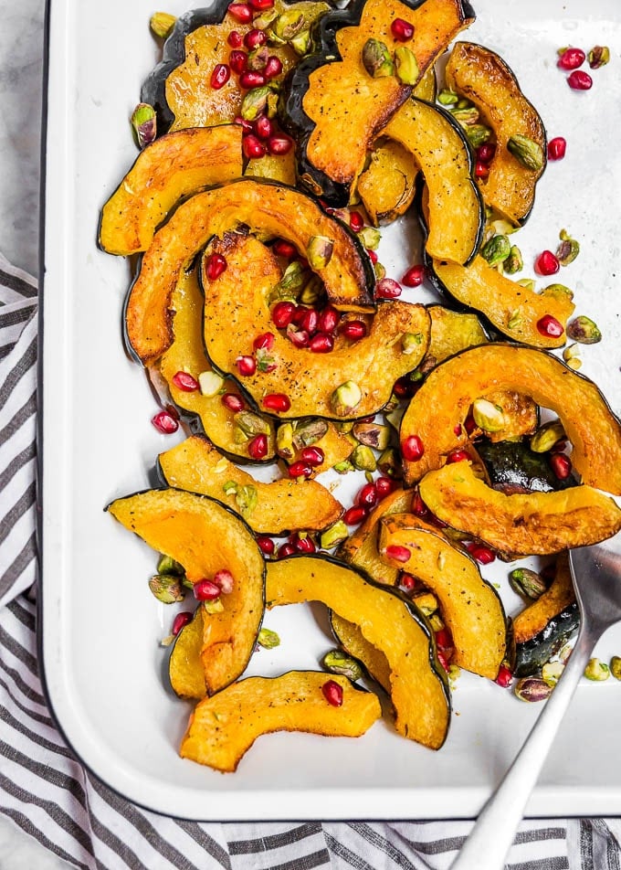 A white sheet pan with roasted acorn squash slices topped with pomegranate arils and pistachios. 