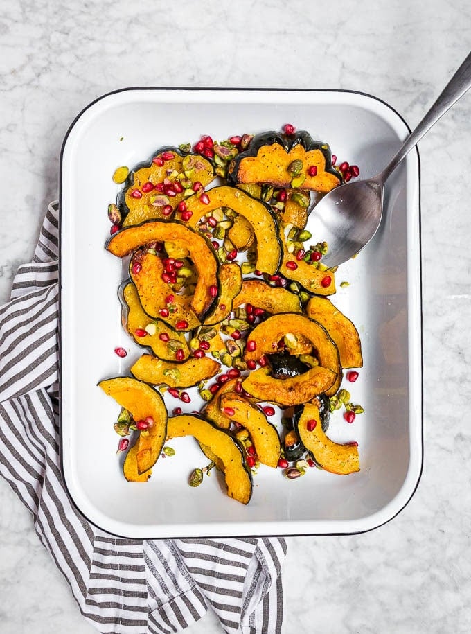 A white sheet pan with slices of acorn squash roasted with pistachios and pomegranate. 