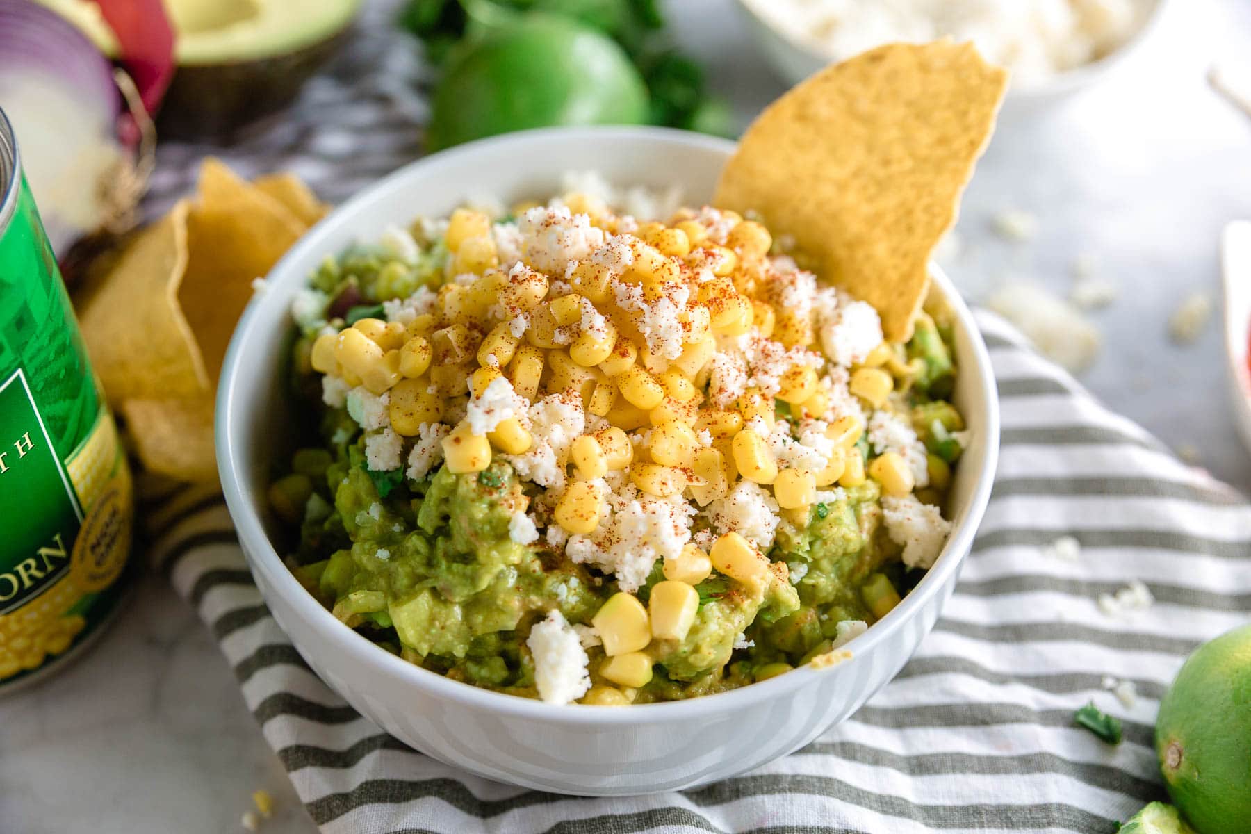 A bowl of corn and cotija cheese guacamole with a tortilla chip and a dusting of paprika on top. 