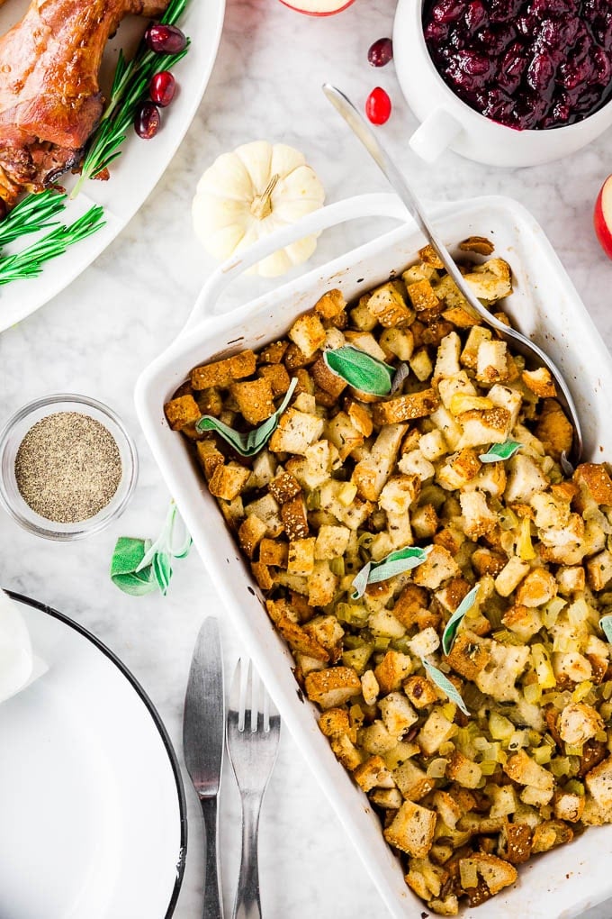 A baking sheet with traditional apple sage gluten-free stuffing with a plate of turkey and a bowl of cranberry sauce and a plate setting ready for Thanksgiving dinner. 