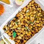 A white baking sheet with classic gluten-free stuffing with celery, onion and apple with a bowl of mashed potatoes and gravy.