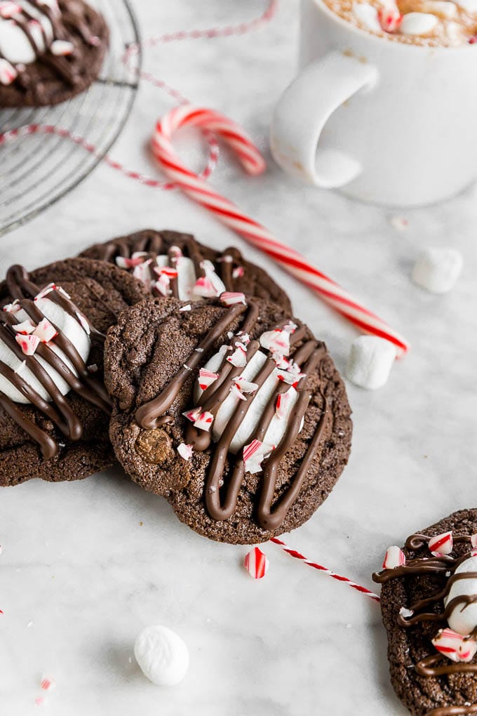 Peppermint Hot Chocolate cookies with marshmallows and candy canes on a table with a cup of hot chocolate and mini marshmallows. 